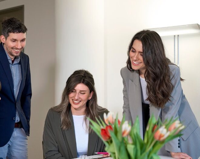 Vier Mitarbeiter in einem Meeting, die um einen Tisch mit Blumen stehen und miteinander sprechen.